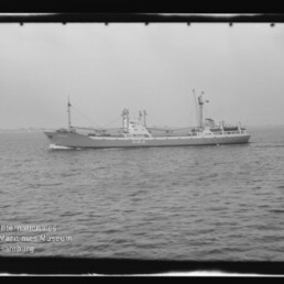 Schwarz-weiß-Foto eines Frachtschiffs auf ruhiger See, mit Wasserzeichen Maritimes Museum Hamburg unten links.
