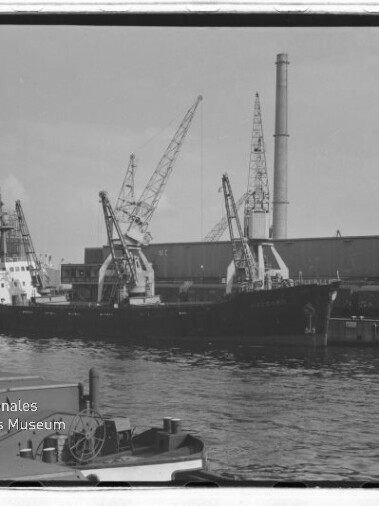Frachtschiff am Industriehafen mit Kränen, Werfthalle und hohem Schornstein; Wasserzeichen: Maritimes Museum Hamburg.