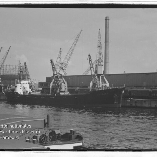 Frachtschiff am Industriehafen mit Kränen, Werfthalle und hohem Schornstein; Wasserzeichen: Maritimes Museum Hamburg.