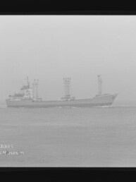 Frachtschiff mit drei Ladekränen fährt bei diesigem Wetter auf ruhiger See, Filmrand und Museumswasserzeichen sichtbar.