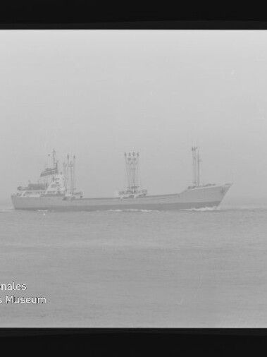 Frachtschiff mit drei Ladekränen fährt bei diesigem Wetter auf ruhiger See, Filmrand und Museumswasserzeichen sichtbar.