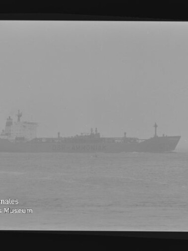 Großes Frachtschiff in dichtem Nebel auf ruhiger See, leicht verschwommen; Maritimes Museum Hamburg-Logo unten links.