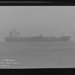 Nebeliger Frachter mit sichtbarem Schriftzug 'AMMONIAK' als Silhouette auf ruhiger See; Filmrand und Museumswasserzeichen.