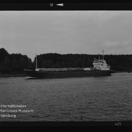 Schwarzweißfoto eines Frachtschiffs auf ruhigem Wasser vor einer Baumreihe; Schriftzug 