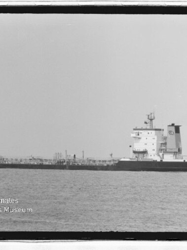 Langes Tankschiff mit achtern liegendem Aufbau auf ruhiger See, Museumslogo unten links.