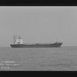 Seitenansicht eines Tankers auf ruhiger See in Schwarzweiß, mit Museumslogo und -schrift unten links.