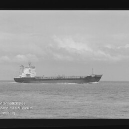 Großes Frachtschiff seitlich auf ruhiger See unter wolkigem Himmel, mit Museumswasserzeichen unten links.