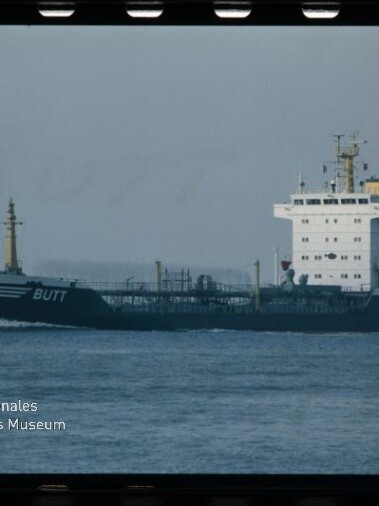 Tanker mit weißen Aufbauten und dunkelblauem Rumpf mit dem Namen BUTT fährt über ruhige See; Museumslogo unten links.
