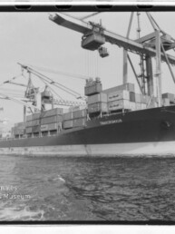 Containerschiff am Kai unter großen Hafenkränen mit gestapelten Containern; Wasserzeichen Internationales Maritimes Museum Hamburg.