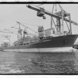 Containerschiff am Kai unter großen Hafenkränen mit gestapelten Containern; Wasserzeichen Internationales Maritimes Museum Hamburg.