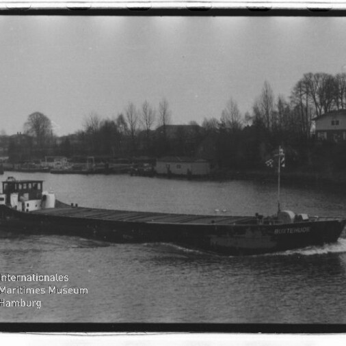 Ein langes Frachtschiff fährt auf einem Fluss, im Hintergrund Ufer mit kahlen Bäumen und Häusern; Museumssignet unten links.