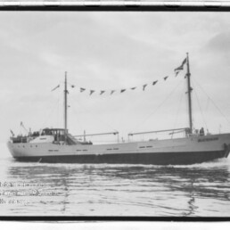 Schwarzweißaufnahme eines zweimastigen Schiffes mit Wimpelgirlande, das ruhig auf glattem Wasser fährt.