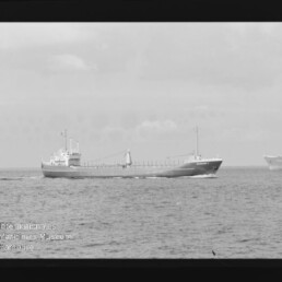 Schwarzweißaufnahme eines Frachtschiffs in Seitenansicht auf ruhiger See mit weiterem Schiff im Hintergrund.