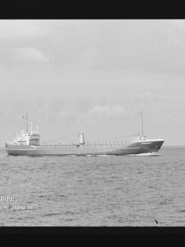 Schwarzweißaufnahme eines Frachtschiffs in Seitenansicht auf ruhiger See mit weiterem Schiff im Hintergrund.