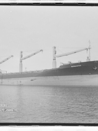 Großes Frachtschiff mit mehreren Ladekränen an einem Industriehafen, Museums-Wasserzeichen links unten.
