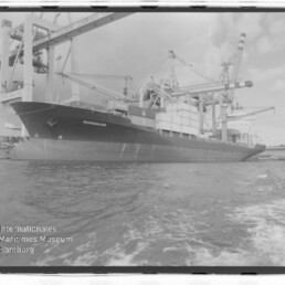 Großes Frachtschiff am Containerterminal unter Kränen, mit Wasserzeichen des Internationalen Maritimen Museums Hamburg.