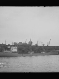 Großes Schiff am Industriehafen vor Lagerhallen und Kränen, Tonnenboje im Vordergrund; Schriftzug 