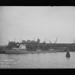 Großes Schiff am Industriehafen vor Lagerhallen und Kränen, Tonnenboje im Vordergrund; Schriftzug 