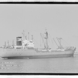 Frachtschiff mit mehreren Ladebäumen und markantem Schornstein auf ruhigem Wasser, Wasserzeichen des Internationalen Maritimen Museums Hamburg.