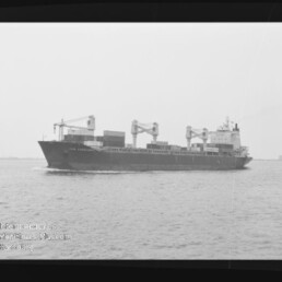 Schwarzweißfoto eines Frachtschiffs mit Bordkränen und Containern auf See; Wasserzeichen Internationales Maritimes Museum Hamburg.