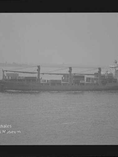 Frachtschiff mit drei Deckskränen auf ruhiger, nebeliger See; Wasserzeichen: Internationales Maritimes Museum Hamburg.