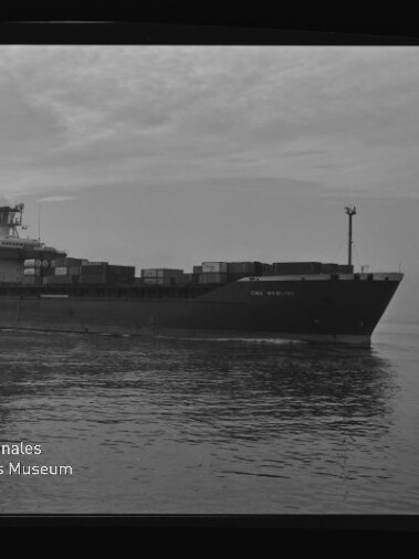 Schwarzweißaufnahme eines Containerschiffs mit gestapelten Frachtcontainern auf ruhiger See, Filmrahmen und Museumswasserzeichen.
