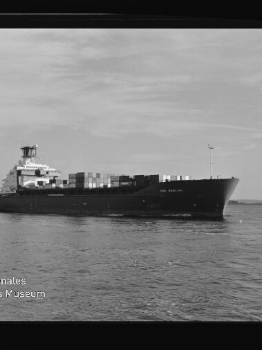 Containerschiff auf ruhigem Wasser, seitliche Ansicht mit Containern; Wasserzeichen: Internationales Maritimes Museum.