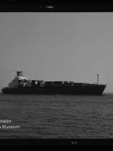 Schwarzweißaufnahme eines Containerschiffs auf ruhiger See, mit Containerstapel und Museumslogo unten links.