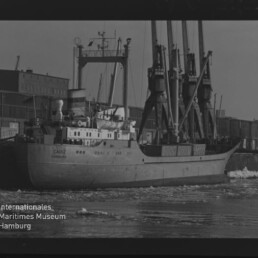 Frachtschiff CADIZ am Kai neben hohen Ladekranen, Eisstücke im Wasser und Museums-Wasserzeichen unten links.