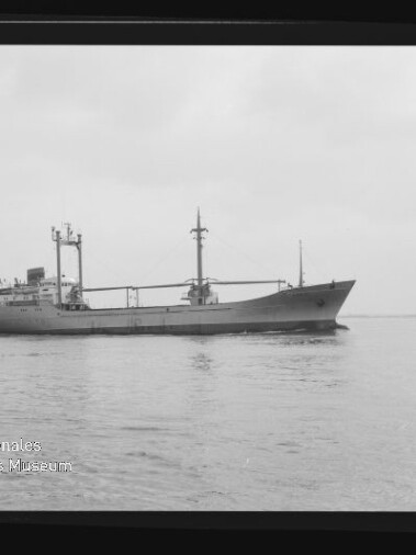 Frachtschiff mit zwei Masten und Ladegeschirr fährt auf ruhigem Wasser; Museumslogo unten links sichtbar.