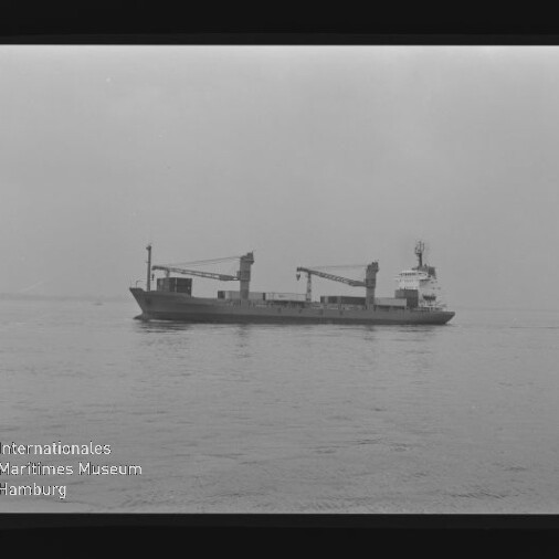 Frachtschiff in Seitenansicht mit zwei Deckskranen auf ruhiger See, schwarzweiß mit Wasserzeichen des Maritimen Museums Hamburg.