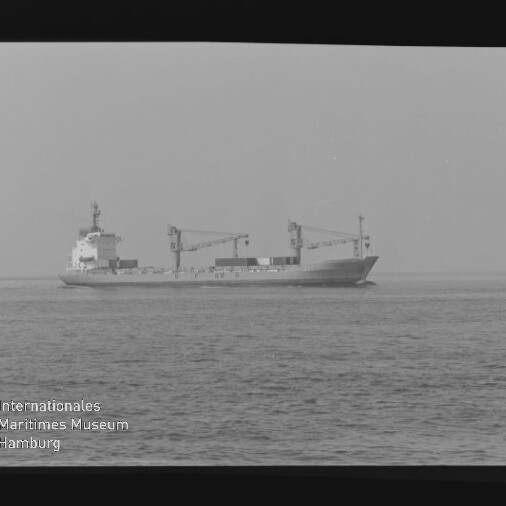 Schwarzweißaufnahme eines Frachtschiffs mit zwei Ladekranen auf ruhiger See, Logo Internationales Maritimes Museum Hamburg unten links.