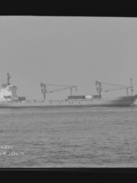 Frachtschiff mit zwei Ladekränen auf ruhiger See, schwarzweißes Foto mit Wasserzeichen Internationales Maritimes Museum Hamburg