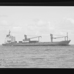 Frachtschiff mit zwei Ladekränen auf ruhiger See in s/w, mit schwarzem Negativrand und Wasserzeichen Maritimes Museum Hamburg.