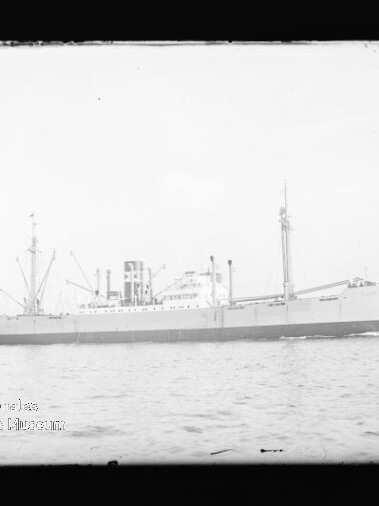 Frachtschiff in Seitenansicht auf ruhiger See mit Ladekränen und Schornstein, schwarzweiß.