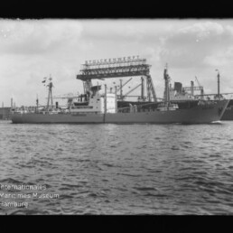 Frachtschiff im Hafen vor einem großen Werftkran mit dem Schriftzug STÜLCKENWERFT und Wellen im Vordergrund.