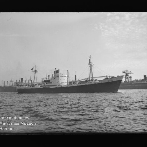 Seitenansicht eines Frachtschiffs im Hafen bei ruhiger See, Hafenkräne im Hintergrund und Wasser im Vordergrund.