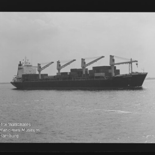 Schwarzweißaufnahme eines Containerschiffs mit vier Ladekränen und gestapelten Containern auf ruhiger See.