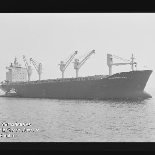 Großes Frachtschiff CALIFORNIA mit Ladekränen und einem Schlepper an ruhiger See, Schwarzweißaufnahme