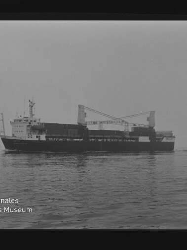 Graustufenfoto eines Frachtschiffs mit zwei Kränen auf ruhiger See; Museumslogo unten links.