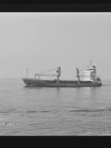Frachtschiff mit zwei Deckskränen auf ruhiger See; unten links sichtbar der Schriftzug Internationales Maritimes Museum Hamburg.