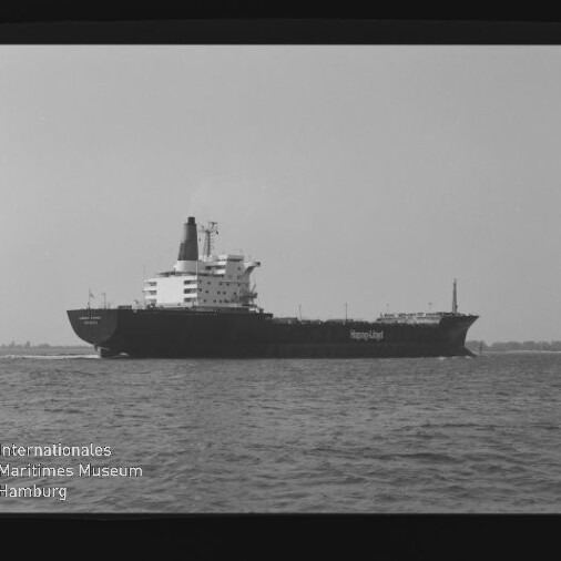 Großes Frachtschiff mit dem Schriftzug Hapag‑Lloyd fährt auf ruhiger See, schwarzweiß-Aufnahme mit Museumswasserzeichen.