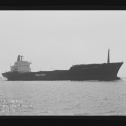 Seitliche Aufnahme eines Frachtschiffs mit Hapag-Lloyd-Logo auf ruhiger See in schwarzweiß; Museumslogo unten links.