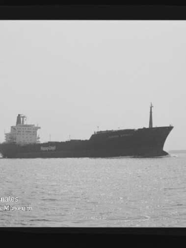 Schwarz-weiß-Foto eines Frachtschiffs in Seitenansicht, das ruhig auf dem Meer vor einem flachen Horizont fährt.