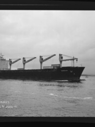 Frachtschiff mit vier Deckskranen auf offener See unter bewölktem Himmel; links unten Schriftzug des Maritimen Museums Hamburg