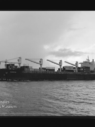 Schwarzweißfoto eines Containerschiffs mit drei Kränen auf dem Meer; Wasserzeichen Internationales Maritimes Museum.