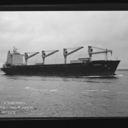 Schwarzweiß-Foto eines Frachtschiffs mit vier Ladekranen, Name CANDIR sichtbar, auf ruhigem Meer mit Museumswasserzeichen.