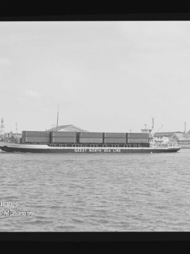 Schwarzweißfoto eines Frachtschiffs mit der Aufschrift GEEST NORTH SEA LINE, beladen mit Containern vor Hafenkränen.