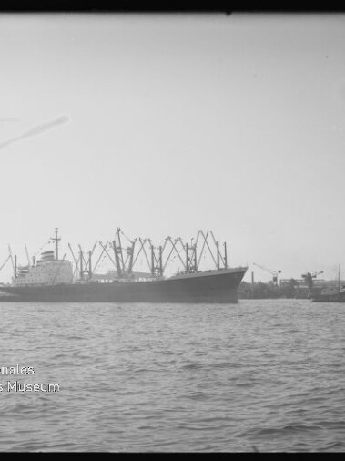 Frachtschiff mit mehreren Ladekränen im Hafen, Wasser im Vordergrund; Wasserzeichen: Internationales Maritimes Museum Hamburg