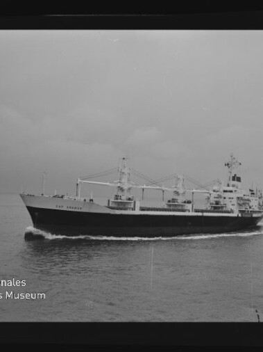 Schwarzweißaufnahme eines Frachtschiffs mit Ladekränen auf ruhiger See, links unten Wasserzeichen Internationales Maritimes Museum Hamburg